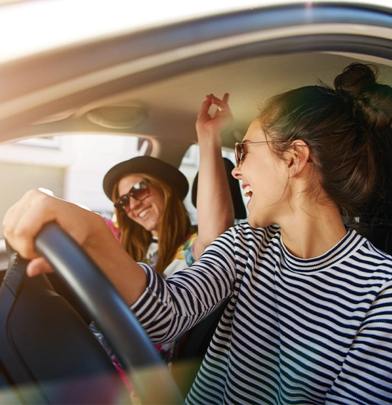 Joyful young women in sunglasses laughing and driving through town, view through open side window