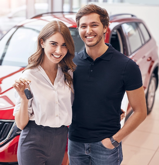 Cheerful man and woman smiling and showing keys while standing near vehicle in contemporary showroom