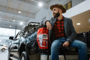 Bearded man in hat and plaid shirt sitting on a new black pickup truck, symbolizing easy business vehicle finance.